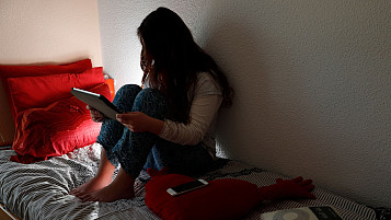 adolescente en la cama sentada usando una tablet