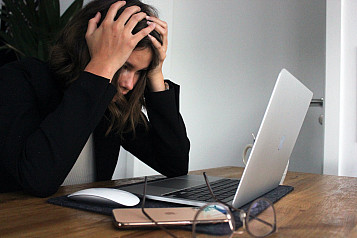 mujer delante de un portátil con las manos en la cabeza mirando agobiada