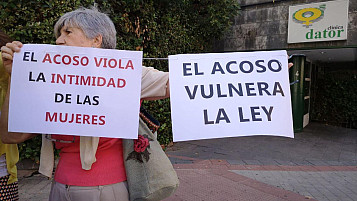 mujer con dos carteles: "el acoso vulnera la intimidad de las mujeres" y "el acoso vulnera la ley"
